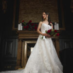 Bride in a lace wedding gown holding red roses, standing before the ornate fireplace at Hutchesons' Hall, Glasgow's Merchant City wedding venue